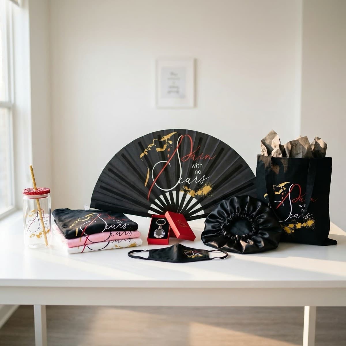 Pain With No Scars merchandise collection — t-shirts, tote bag, hand fan, crystal keychain, satin bonnet, face mask, and faith tumbler